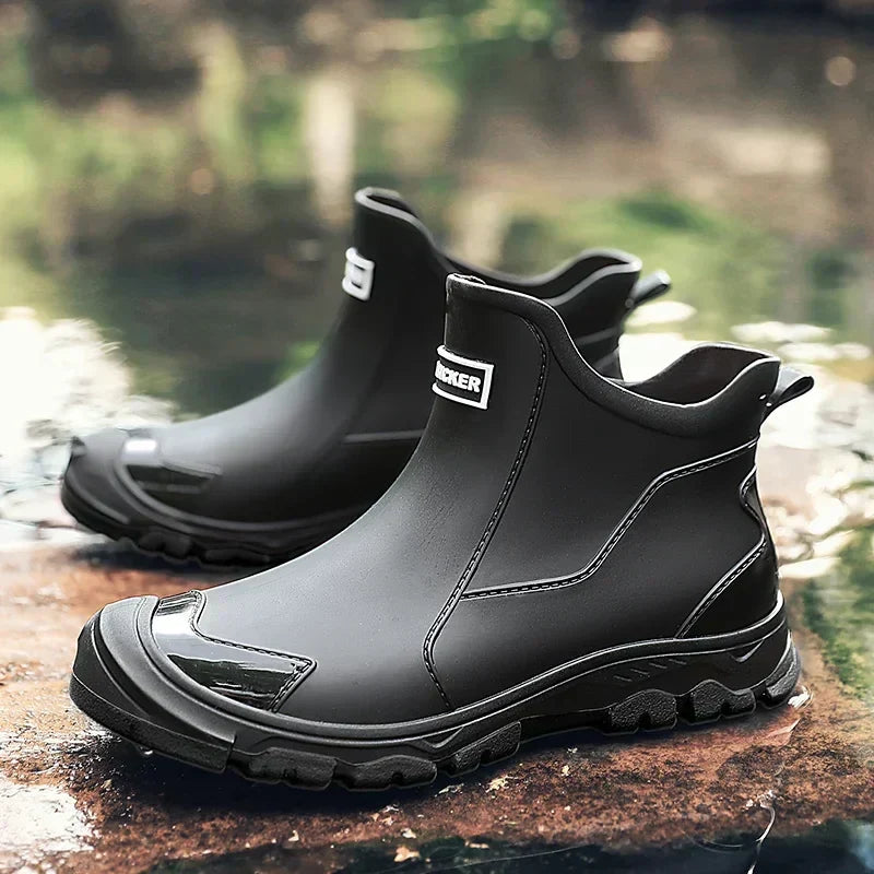 Black waterproof ankle rain boots with a rugged treaded sole, slip-on design, and rear pull tab, set on a wet surface.
