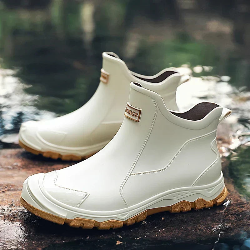 White waterproof ankle rain boots with a rugged tan tread sole and rear pull tab, set on a wet outdoor surface.