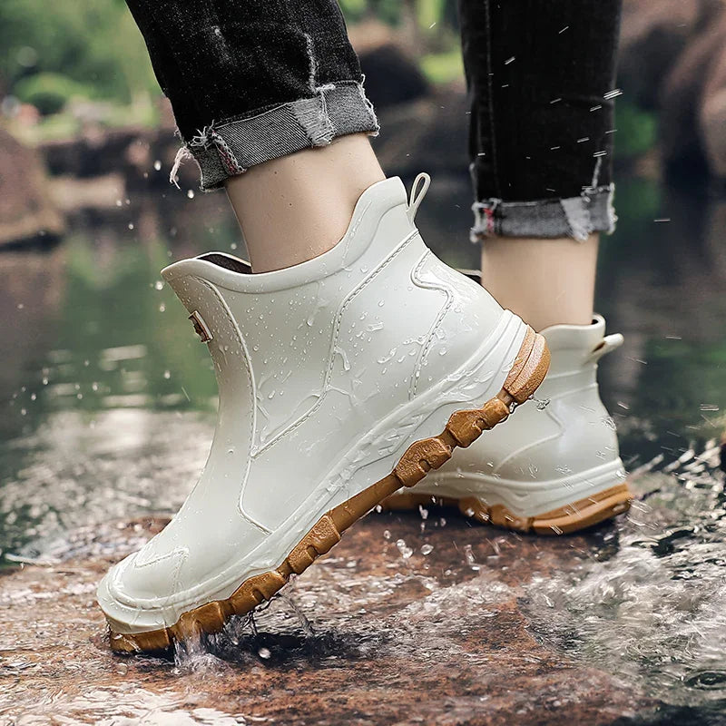 White waterproof ankle rain boots with a rugged brown tread sole and rear pull tab, worn in shallow water.