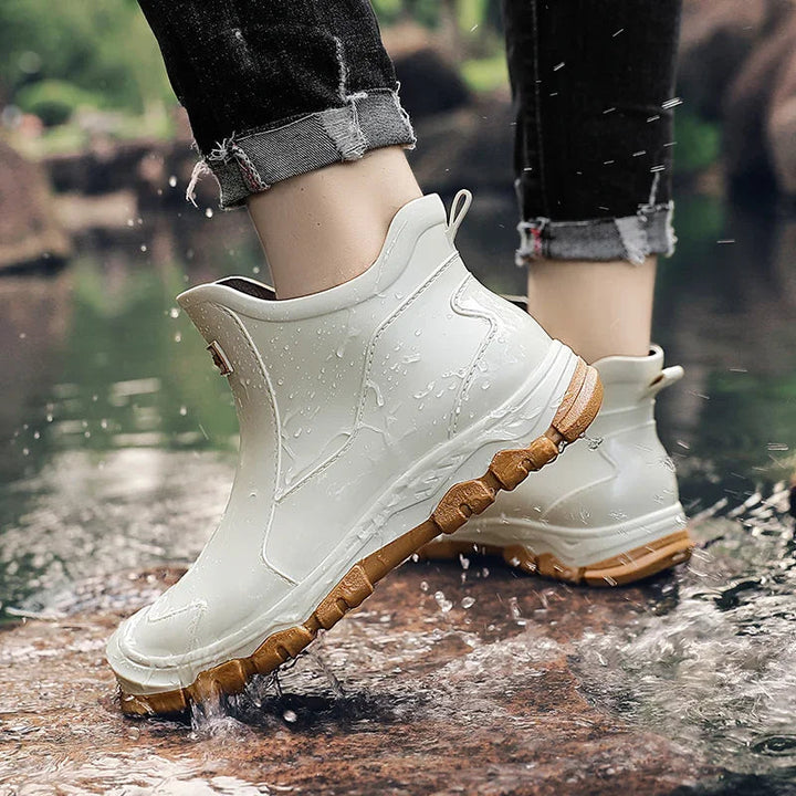 White waterproof ankle rain boots with a rugged brown tread sole and rear pull tab, worn in shallow water.