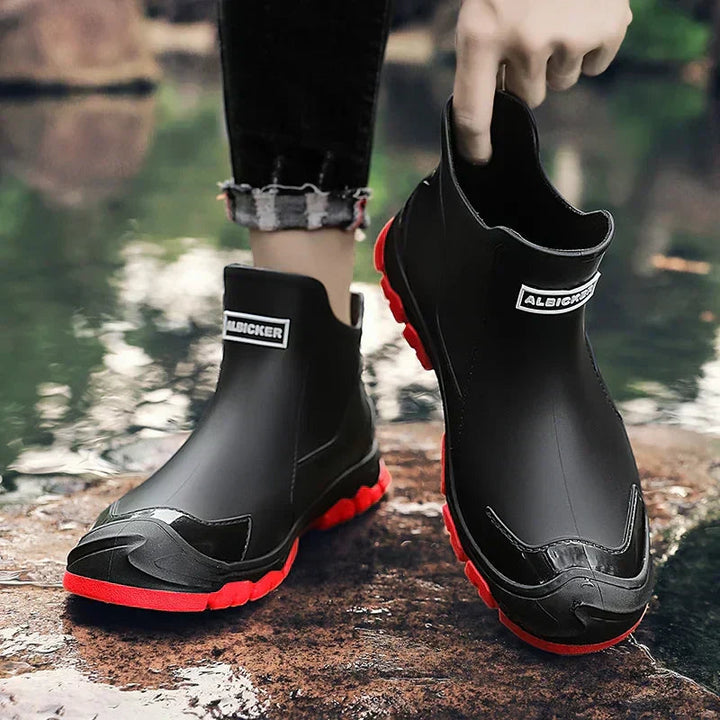 Black waterproof ankle rain boots with a vibrant red lug sole and a rear pull tab for easy slip-on wear.
