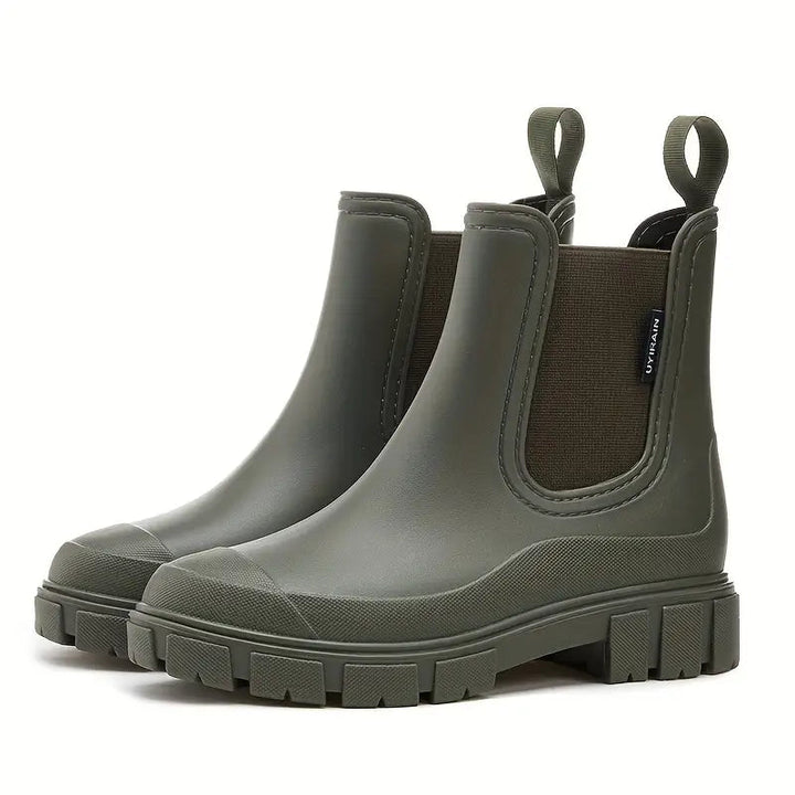 Olive green waterproof Chelsea rain boots with a chunky lugged sole, side elastic gussets, and pull tabs.