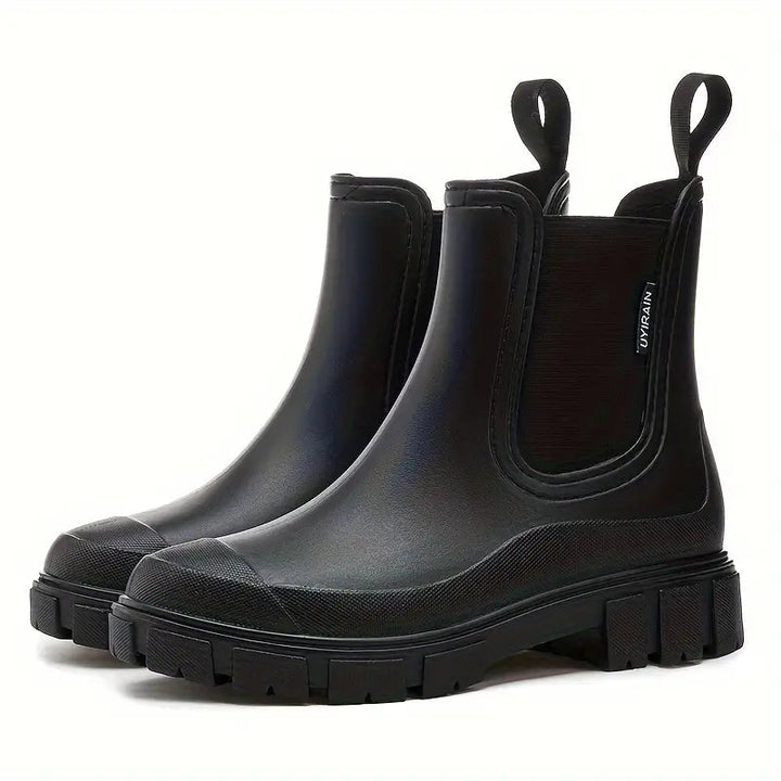 Black waterproof Chelsea rain boots with a chunky lugged sole, side gussets, and pull tabs on a white background.