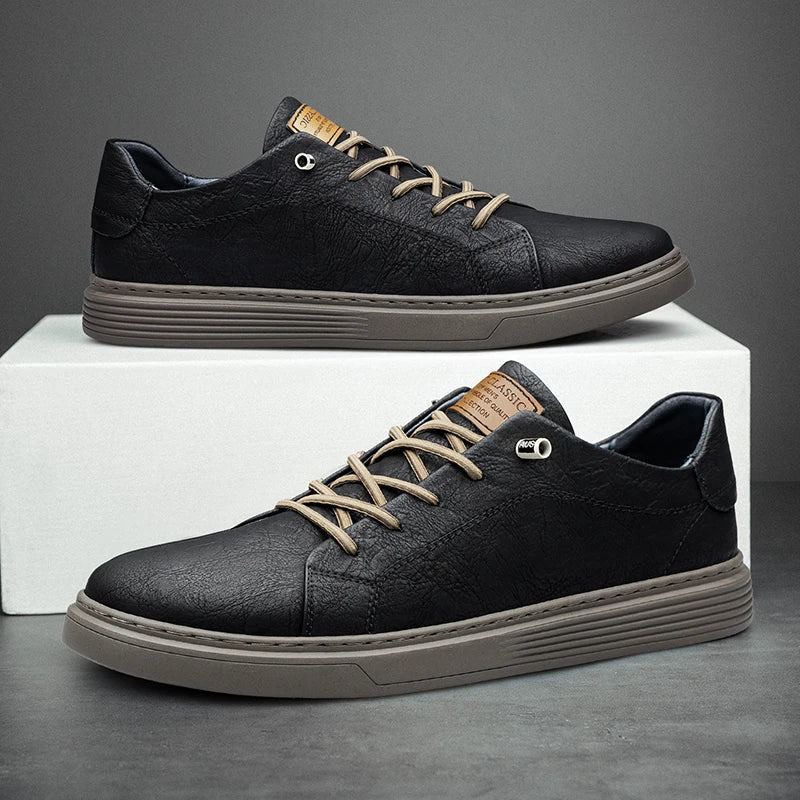 Black textured leather low-top trainers with beige laces and a ribbed grey sole, featuring a tan tongue label.
