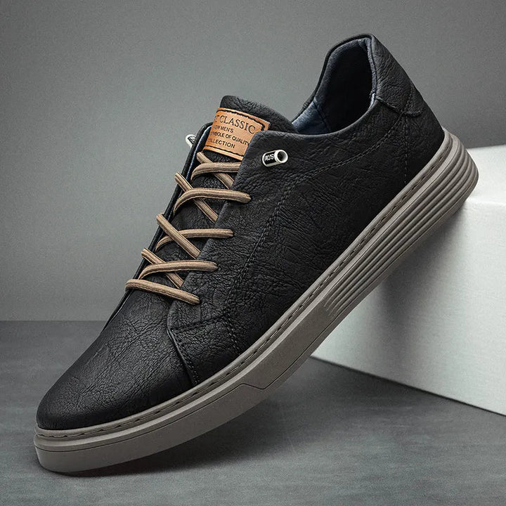 Black textured leather low-top trainers with tan laces, a brown tongue label, and a thick grey contrast sole.
