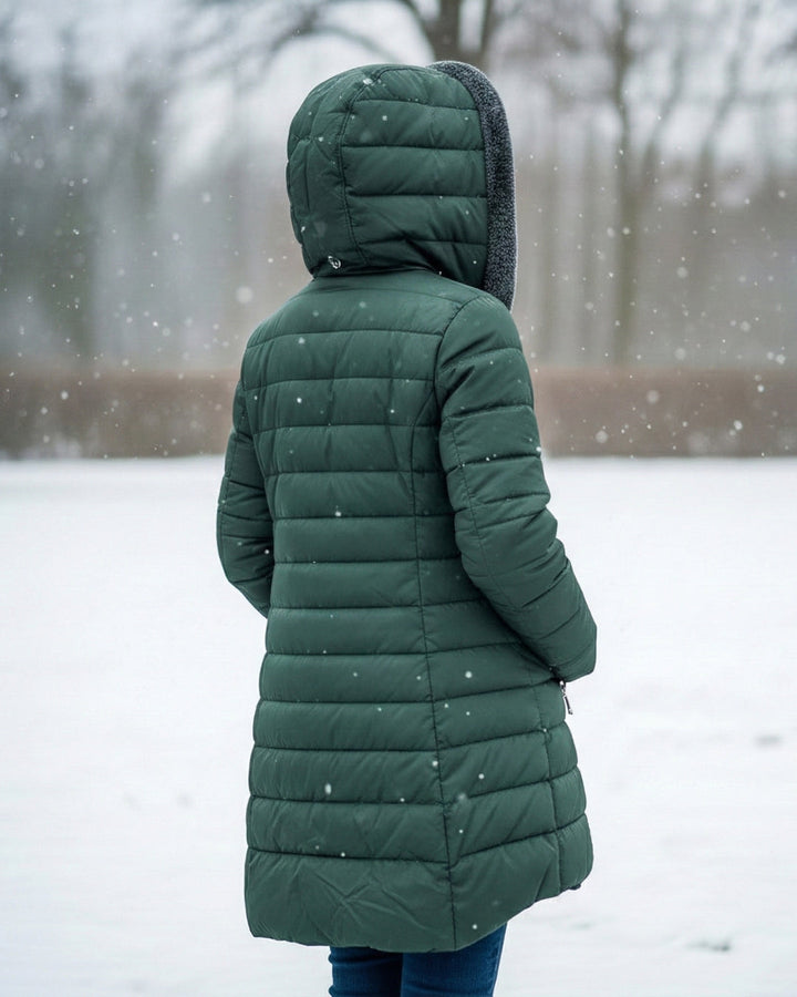 Woman wearing a dark green, longline quilted puffer coat with a cozy fleece-lined hood in a snowy outdoor setting.