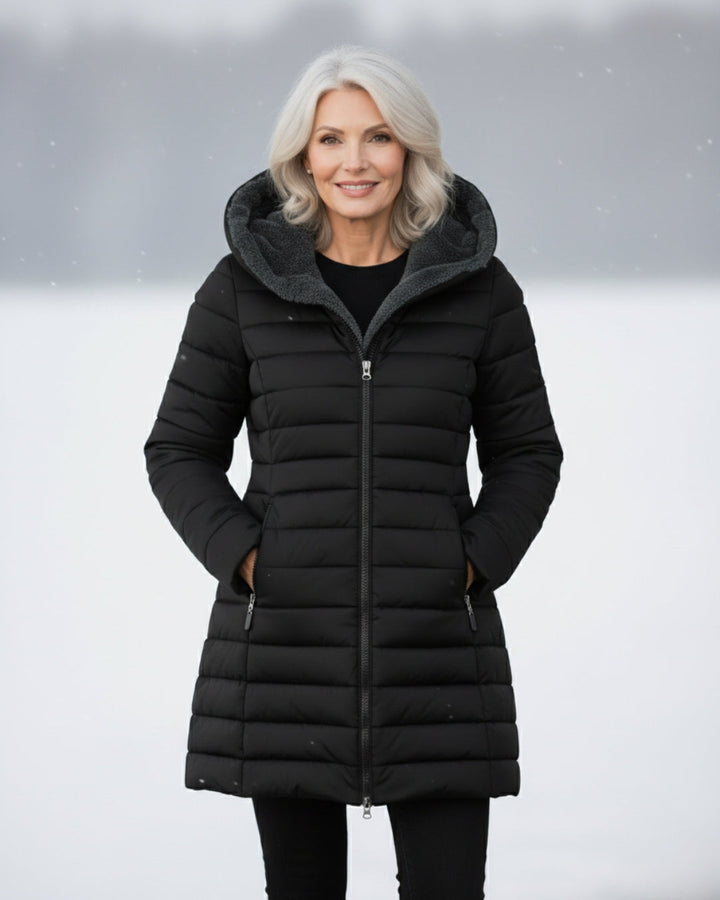 Woman wearing a black longline quilted puffer coat with a cozy fleece-lined hood in a snowy outdoor setting.