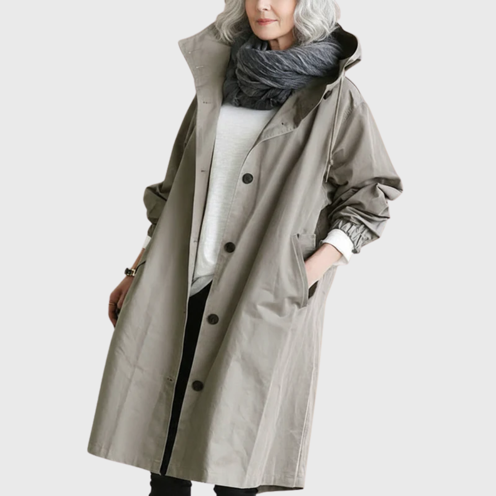Taupe oversized waterproof raincoat with a hood, button-front closure, and longline silhouette worn over a white top.