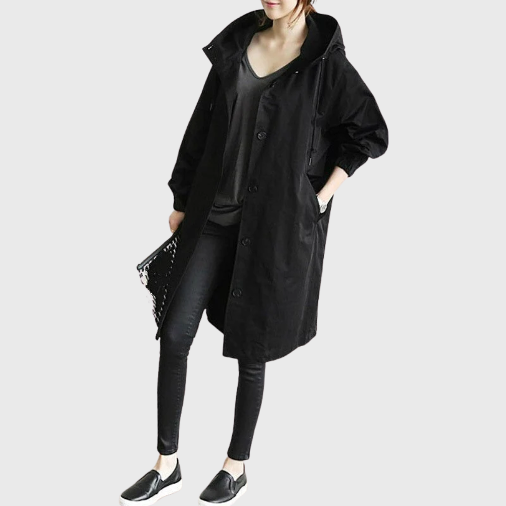 Black oversized waterproof raincoat with a hood, button-front closure, and longline silhouette worn over black skinny jeans.