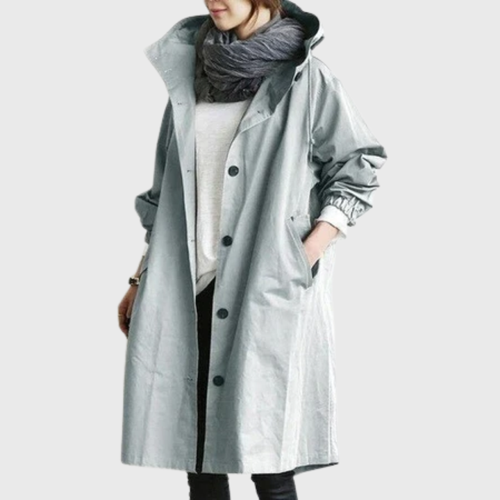 Woman wearing an oversized, light grey waterproof raincoat with a hood, button-front closure, and side pockets.