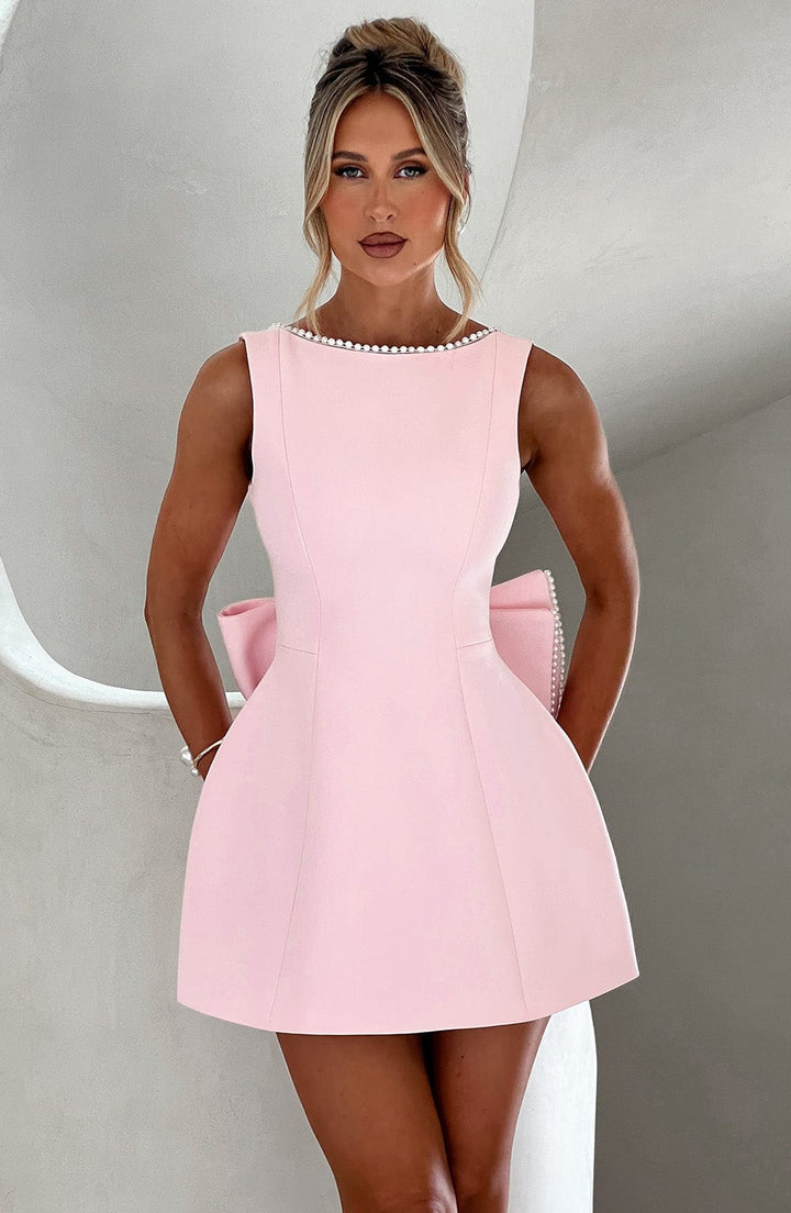 Sleeveless light pink mini dress featuring a pearl-trimmed neckline and a large structural bow detail at the back.