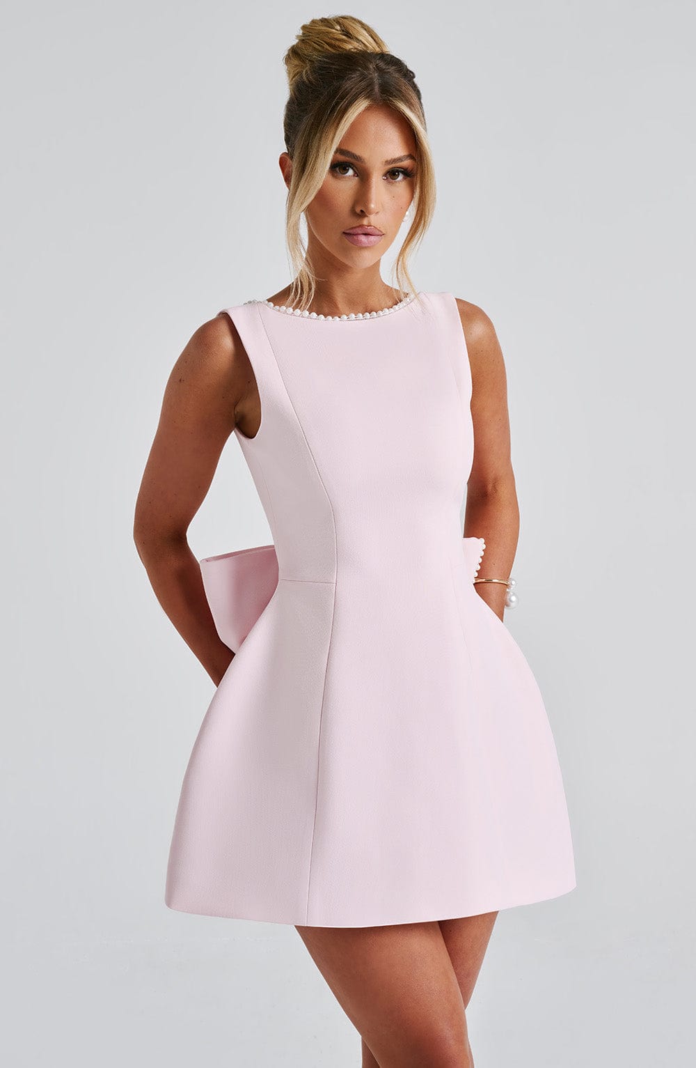 Light pink sleeveless mini dress with a pearl-trimmed neckline and a structured fit-and-flare silhouette.