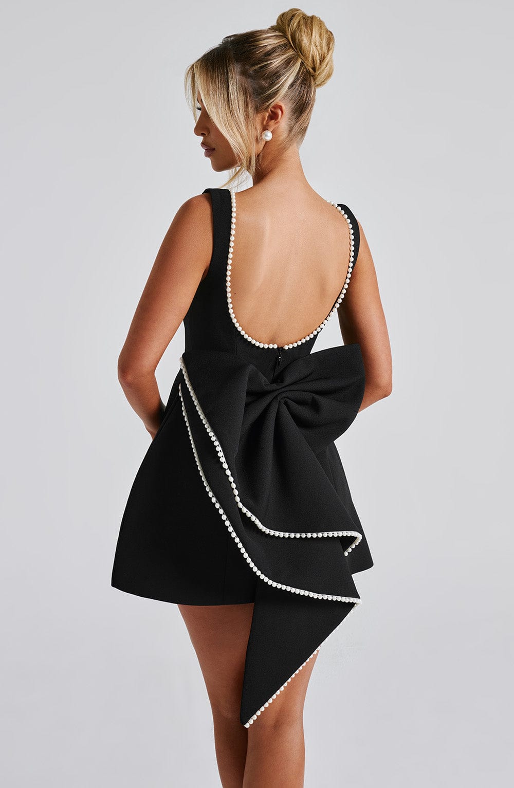 Black sleeveless mini dress featuring a pearl-trimmed scoop back and a large structured bow detail.