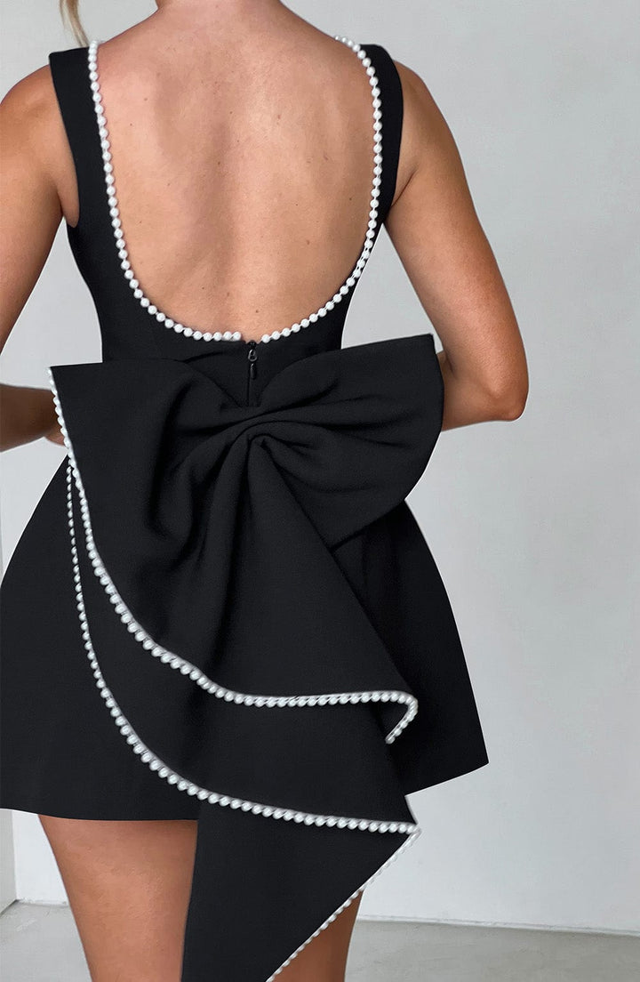 Sleeveless black mini dress with a pearl-trimmed scoop back and a large structural bow detail.