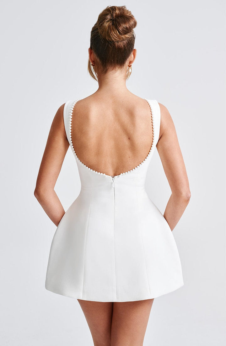 Back view of a white sleeveless mini dress with a low scoop back and delicate pearl trim along the neckline.