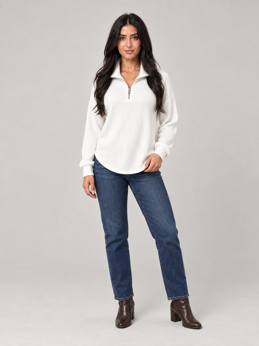 Model wearing a white relaxed-fit waffle knit half-zip jumper with a funnel neck, styled with blue jeans and brown boots.