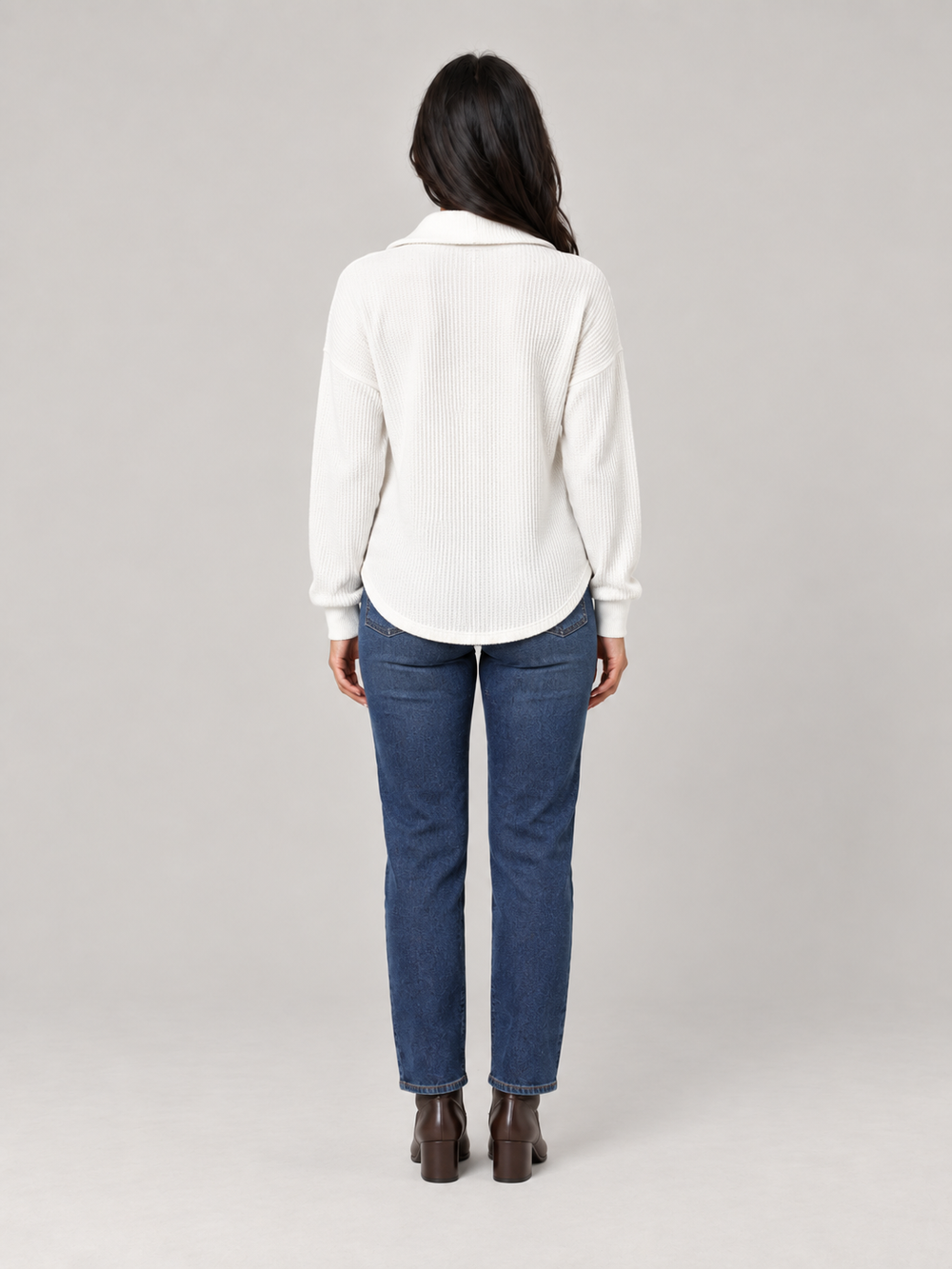 Back view of a white relaxed-fit waffle knit half-zip jumper paired with blue jeans and brown boots.