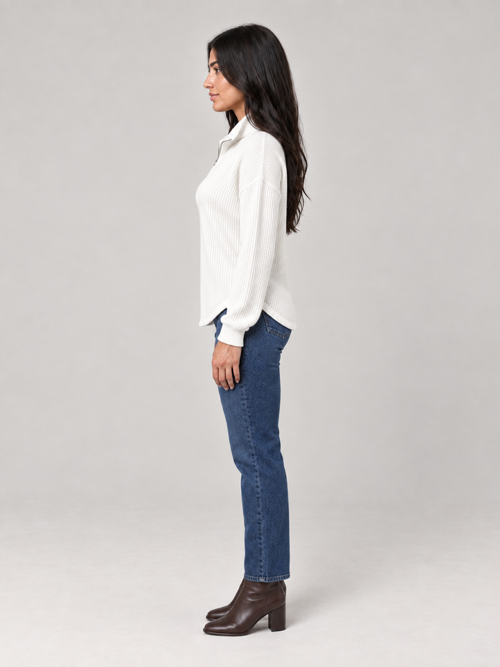Woman wearing a white relaxed-fit waffle knit half-zip jumper with a funnel neck, styled with blue jeans and boots.
