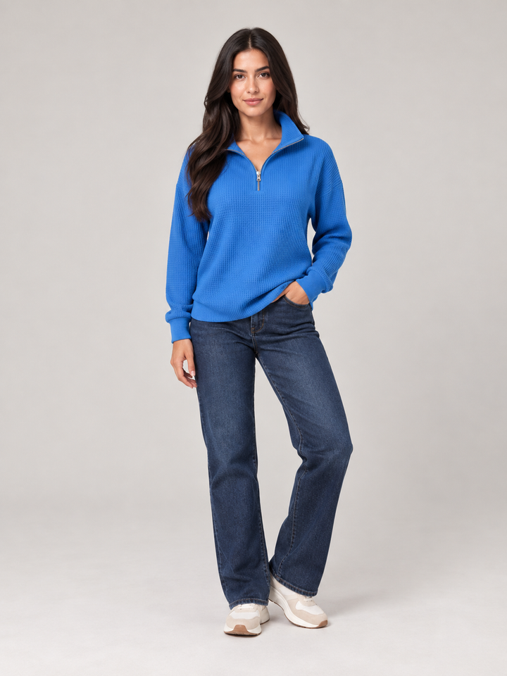 Model wearing a vibrant blue relaxed-fit waffle knit jumper with a sporty half-zip funnel neck and long sleeves.