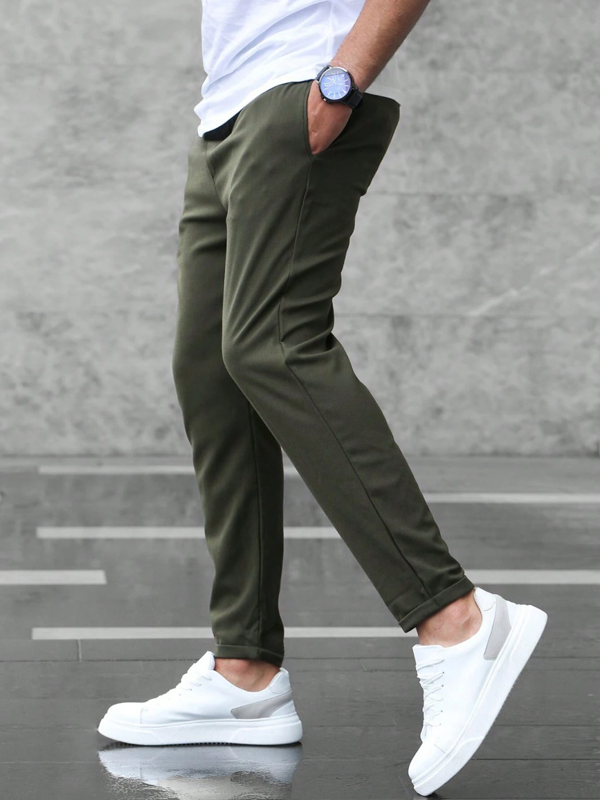 Olive green slim-fit joggers with a tapered leg, side pockets, and elasticated waist worn with white sneakers.