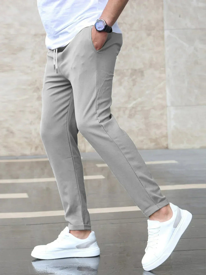 Men wearing slim-fit light grey drawstring joggers with side pockets and a tapered silhouette paired with white sneakers.