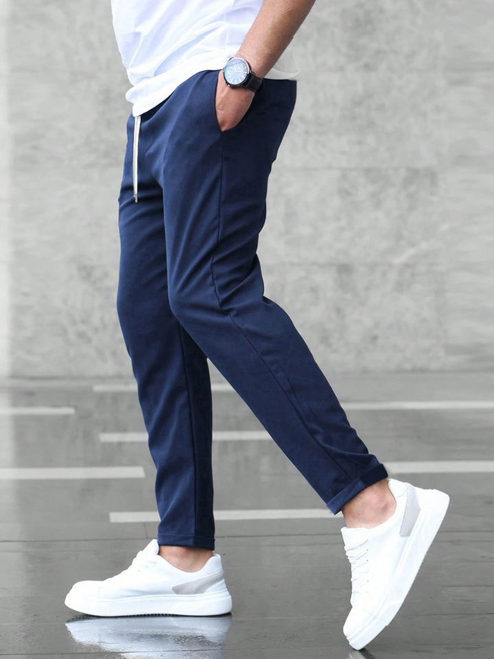 Men wearing navy blue slim-fit joggers with an elasticated drawstring waist and side pockets paired with white sneakers.