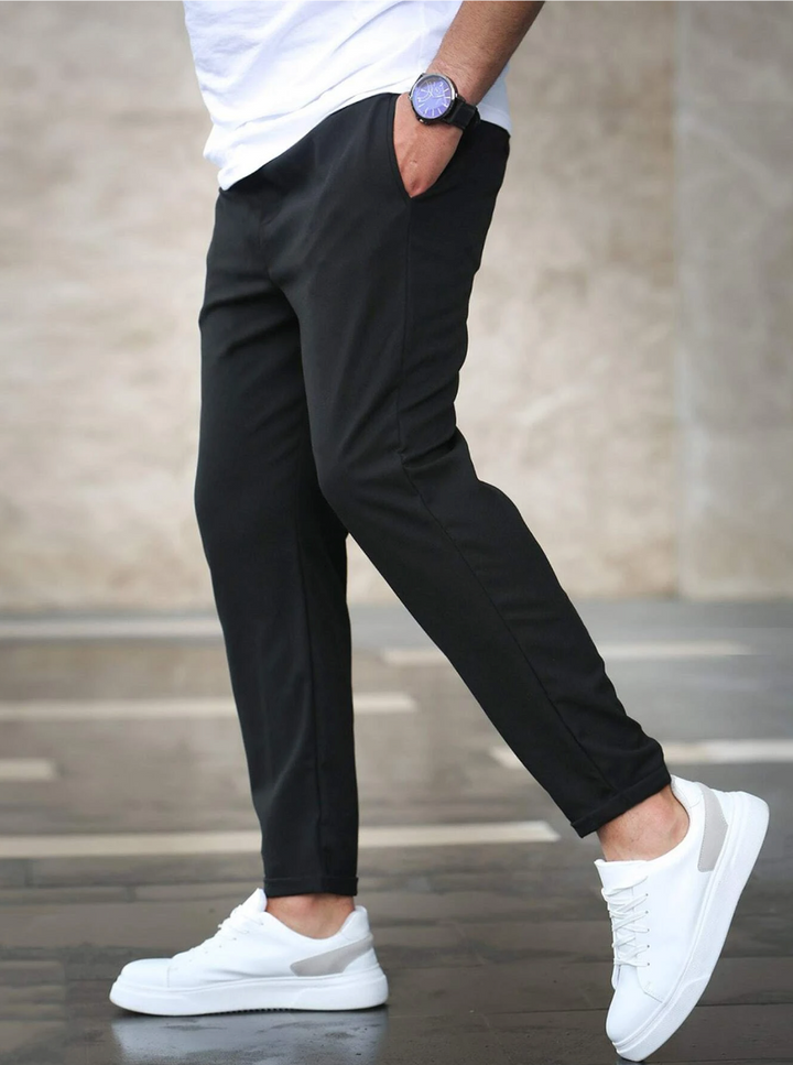 Men's black slim-fit joggers with a drawstring waist and side pockets, styled with a white t-shirt and sneakers.