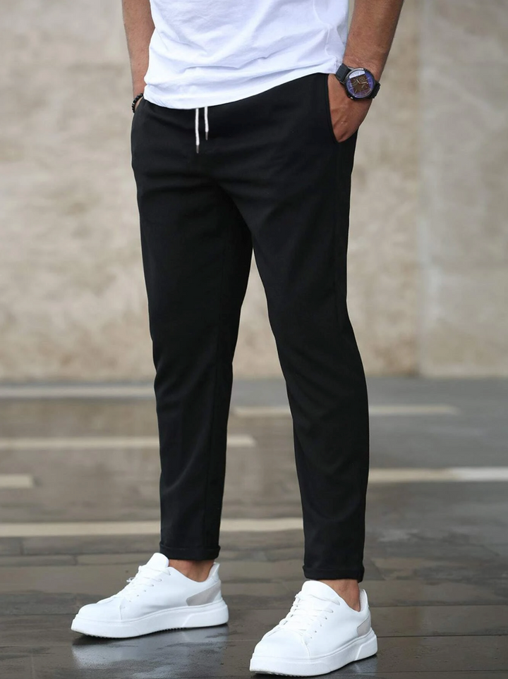 Men's slim-fit black joggers with an elasticated drawstring waist and side pockets, styled with a white t-shirt and sneakers.