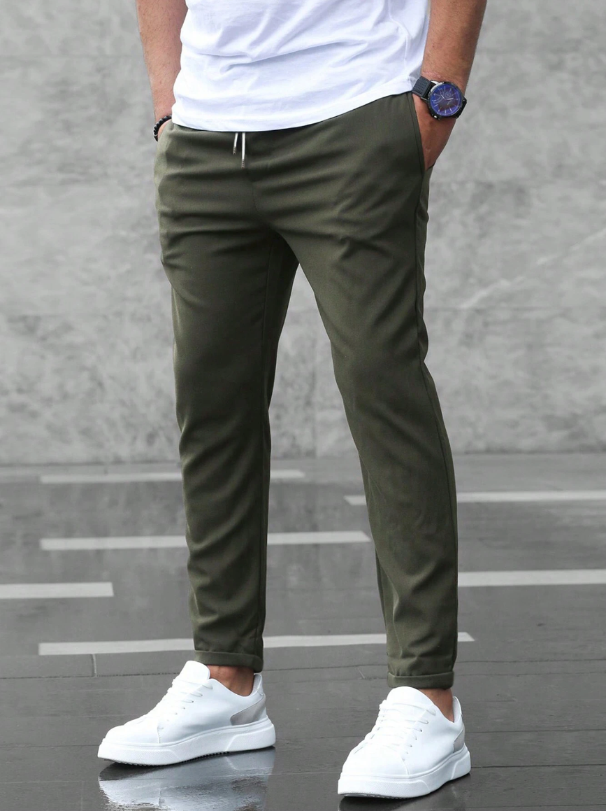 Olive green slim-fit men's joggers featuring an elasticated drawstring waist and side pockets, styled with white sneakers.