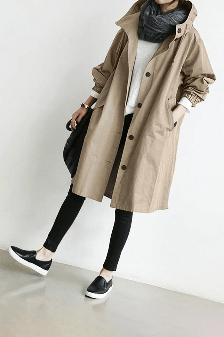 Beige longline hooded windbreaker with button front, elasticated cuffs, and side pockets worn over black leggings.
