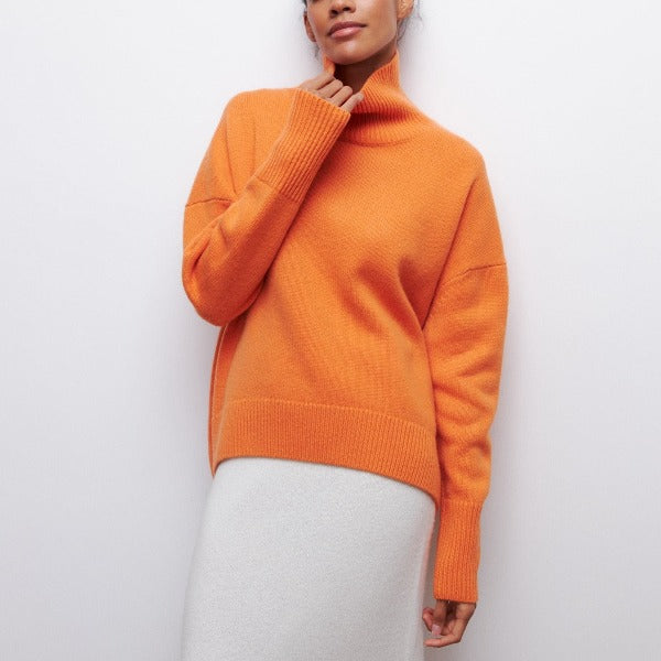 Model wearing a vibrant orange oversized turtleneck jumper with dropped shoulders and ribbed cuffs in a soft knit fabric.