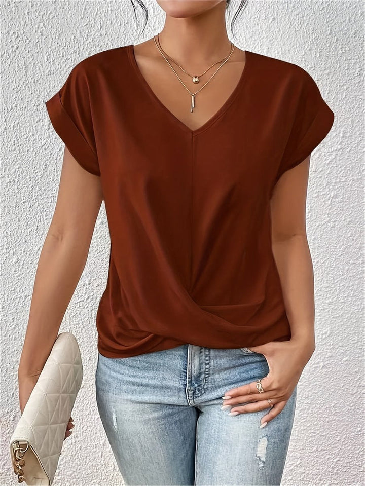 Rust-colored V-neck top with cap sleeves and a flattering twist hem detail, styled with light wash jeans.