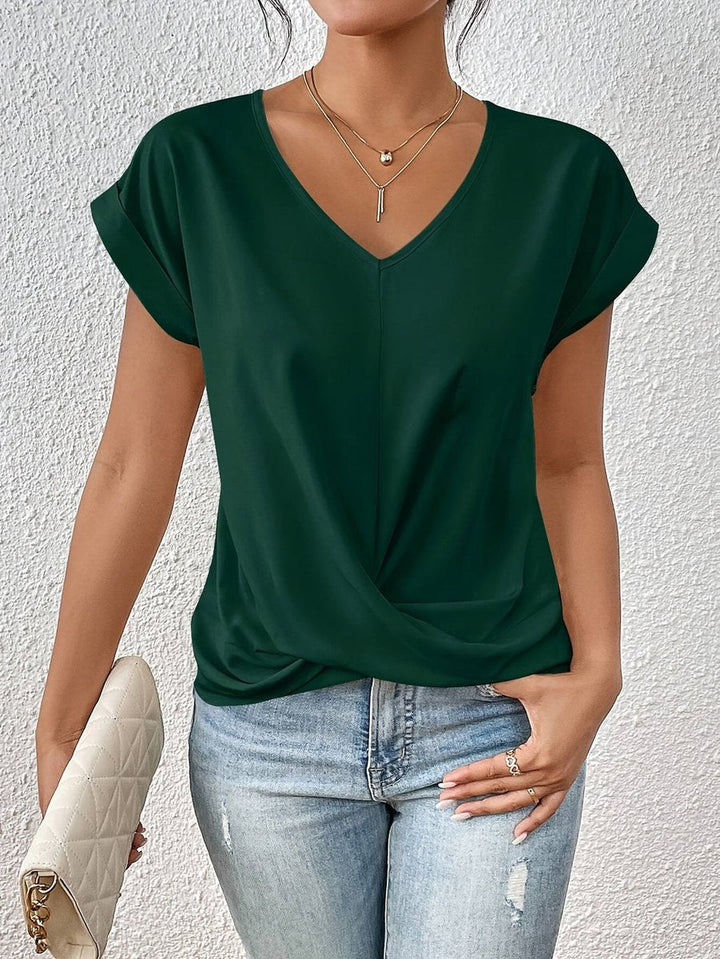 Dark green V-neck top with cap sleeves and a flattering twist hem detail, styled with light wash jeans.