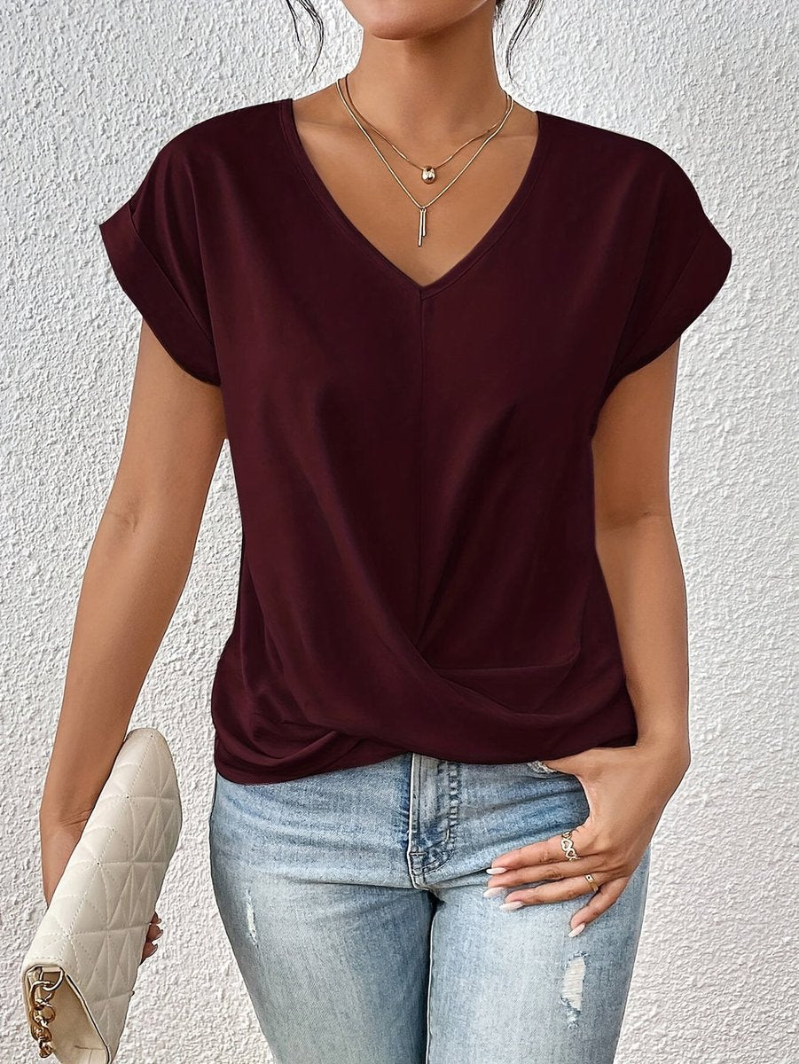 Burgundy V-neck top with cap sleeves and a flattering twist hem detail, styled with light wash distressed jeans.