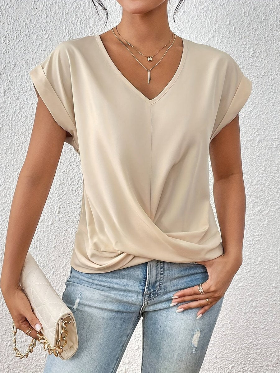 Beige V-neck top with cap sleeves and a flattering twist hem detail, styled with light wash jeans and a clutch.