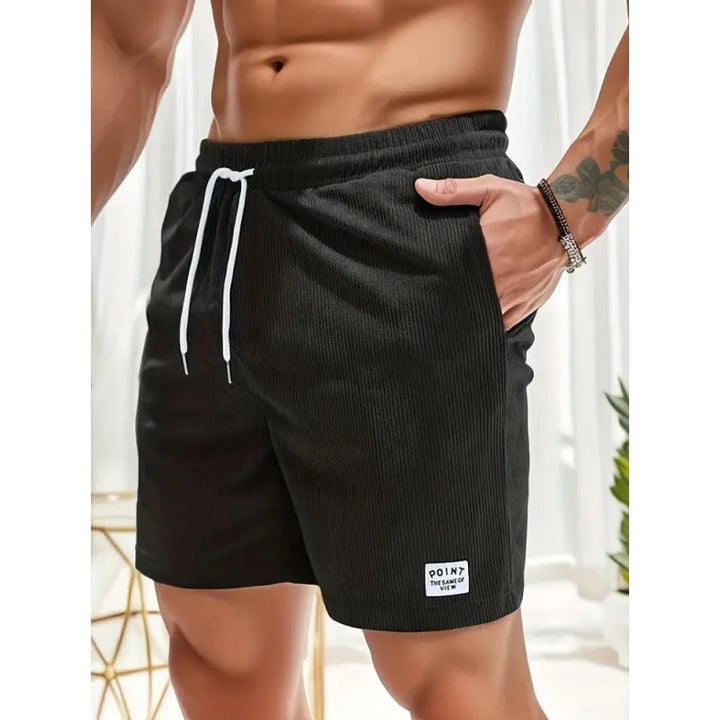 Black textured drawstring shorts with a white waist tie, side pockets, and a small logo patch on the hem.