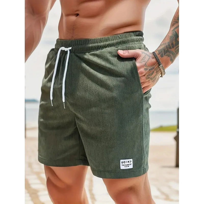 Olive green corduroy drawstring shorts with a white waist tie, side pockets, and a small logo patch on the hem.