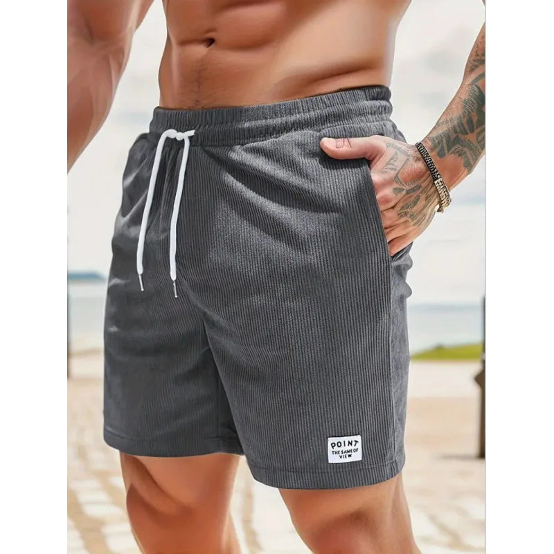 Men's charcoal grey corduroy drawstring shorts with side pockets and a small branded patch on the hem.