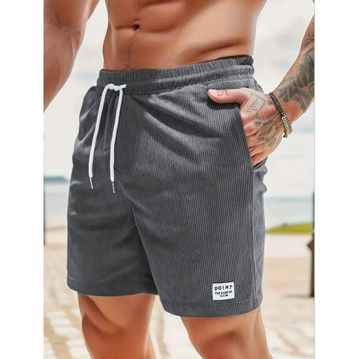 Men's charcoal grey corduroy drawstring shorts with side pockets and a small branded patch on the hem.