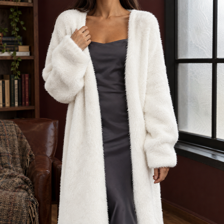 Woman wearing a white, longline plush knit cardigan with an open front and voluminous sleeves over a dark slip dress.
