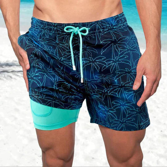 Men's navy blue swim shorts with palm tree print, drawstring waist, and a contrasting teal built-in liner with pocket.