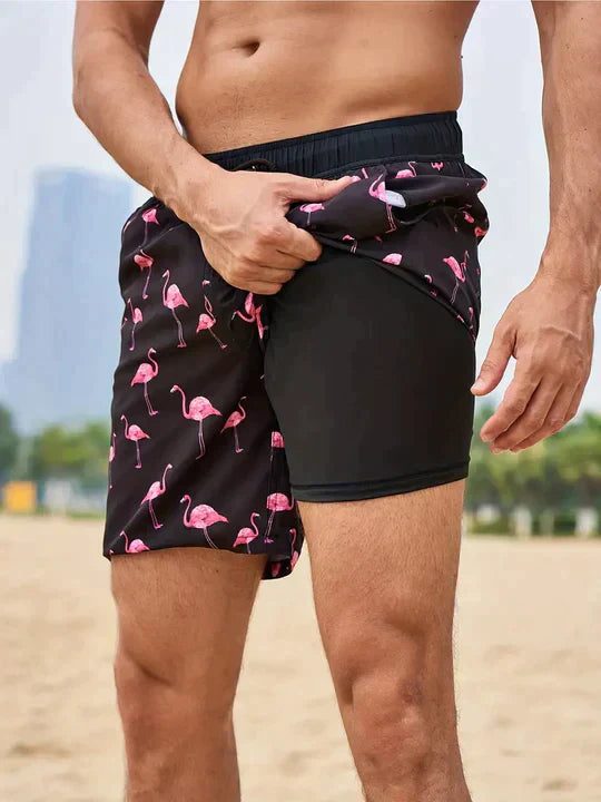 Black swim shorts with pink flamingo print, featuring an elastic drawstring waist and a supportive black inner liner.
