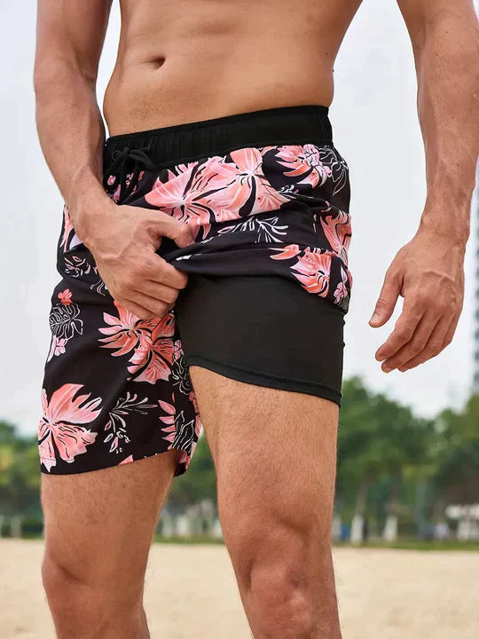 Men's black swim shorts featuring a pink floral print, elastic drawstring waistband, and a supportive black inner liner.