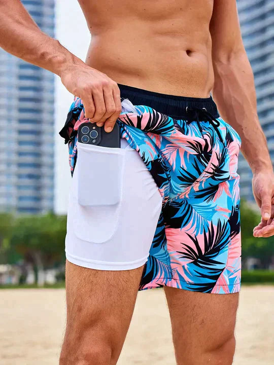 Men's swim shorts with blue and pink tropical print, drawstring waist, and white liner featuring a side phone pocket.