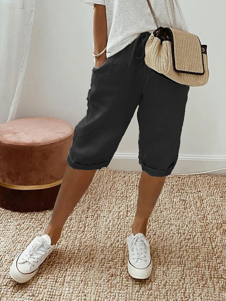 Women's Georgia black linen drawstring shorts with side pockets, styled with a white tee and woven bag.