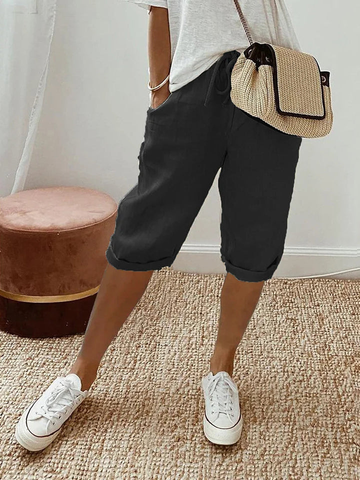 Women's Georgia black linen drawstring shorts with side pockets, styled with a white tee and woven bag.
