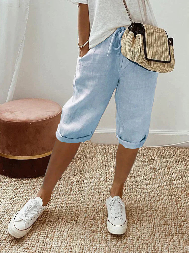 Women's light blue linen drawstring shorts with rolled cuffs, side pockets, paired with a white tee and sneakers.