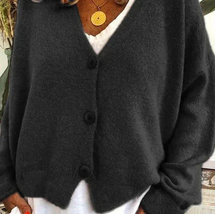 Charcoal grey V-neck knit cardigan with a button-down front and relaxed fit, layered over a white top.