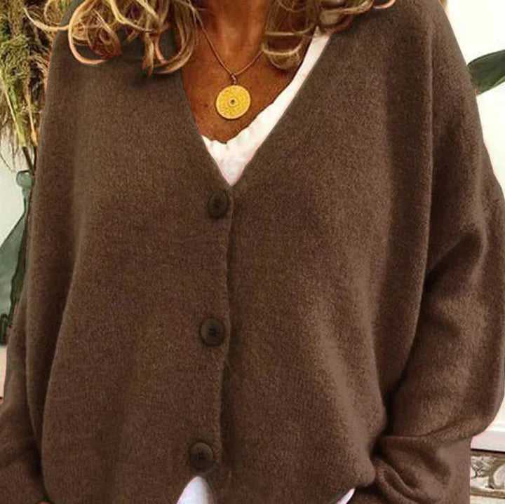 Soft brown knit V-neck cardigan with a button-front closure and relaxed fit worn over a white top.