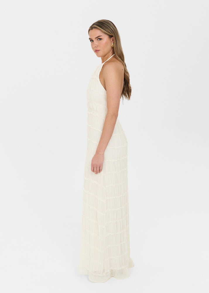 Cream-colored maxi dress with a halter neckline, open back, and tiered textured fabric, shown from the side.